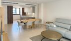 Heller Wohn-Essbereich mit moderner Küche, Holztisch und grauem Sofa in exklusiver Neubauwohnung Palma
