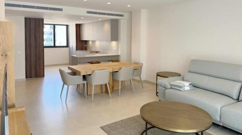 Heller Wohn-Essbereich mit moderner Küche, Holztisch und grauem Sofa in exklusiver Neubauwohnung Palma