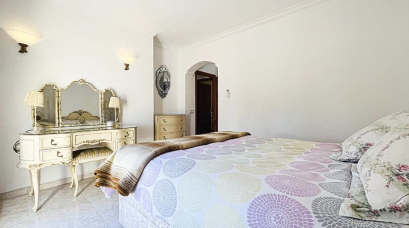 Elegantes Schlafzimmer der Strandvilla in Cala Vinyes mit antikem Schminktisch, Doppelbett und Bogentür.