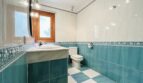 Helles Badezimmer der Villa in Cala Vinyes mit blauen Fliesen, Waschbecken, WC und Holzfenster.