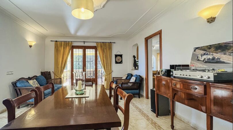 Helles Wohnzimmer mit Holzmöbeln, blauer Couch, Vinylspieler und Terrassenausgang in Villa Cala Vinyes