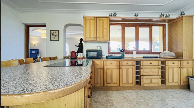 Geräumige Küche der Villa in Cala Vinyes mit Holzfronten, Granitinsel und großem Fenster mit Naturlichteinfall.