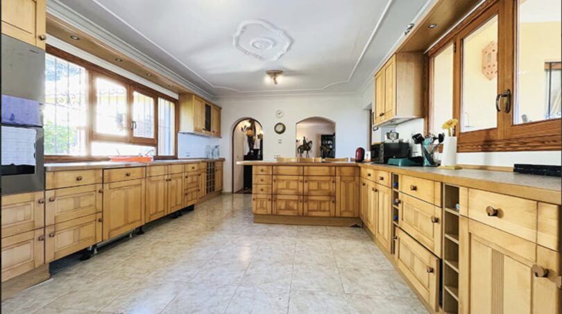 Geräumige Küche der Villa in Cala Vinyes mit Holzschränken, Kücheninsel und Fliesenboden.