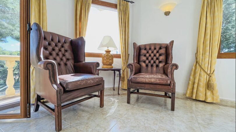 Elegantes Lesezimmer der Villa in Cala Vinyes mit zwei Chesterfield-Ledersesseln und goldenen Vorhängen.