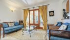 Wohnzimmer der Villa in Cala Vinyes mit blauen Sofas, Glastisch und goldenen Vorhängen vor Terrassentür.