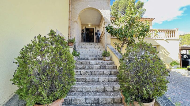 Steintreppe mit Rundbogen-Eingang, flankiert von Büschen – Außenbereich der exklusiven Villa in Cala Vinyes.