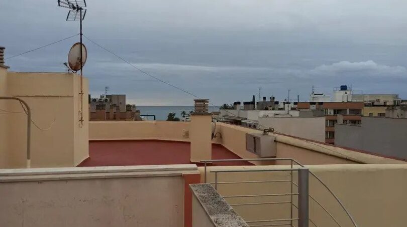 Dachterrasse der Maisonette in El Molinar mit Meerblick, Geländer und umliegenden Stadtdächern unter bewölktem Himmel.