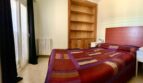 Schlafzimmer des Chalets in Marratxí mit Doppelbett, Holzregal, Heizkörper und Balkontür mit dunklen Vorhängen.
