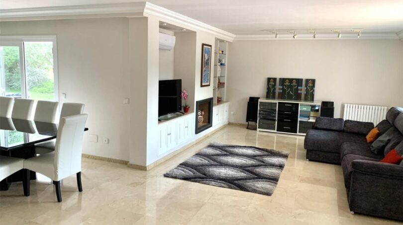 Helles Wohnzimmer mit Marmorboden, dunklem Sofa, TV-Einheit und Essbereich im Chalet Es Garrovers, Marratxí.