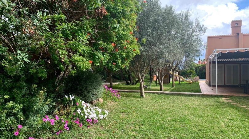 Gepflegter Garten des Chalets in Es Garrovers mit Olivenbäumen, Blumenrabatten und Spielplatz