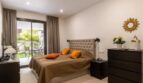 Bright bedroom of the ground-floor apartment La Vileta with double bed, orange cushions and terrace access to the garden.