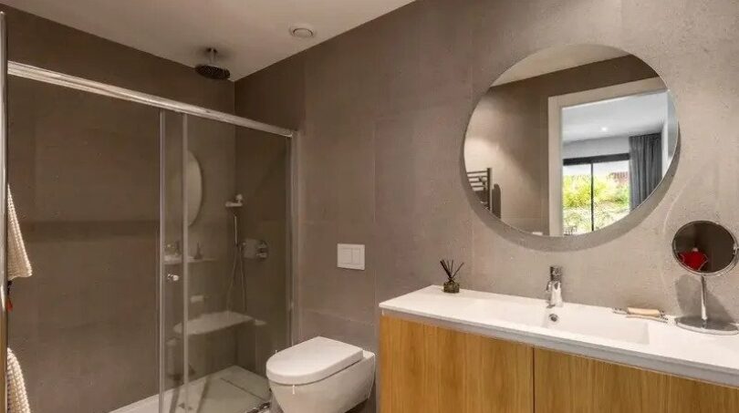 Modern bathroom of the new ground-floor apartment in La Vileta with glass shower, wall-hung WC and round mirror.
