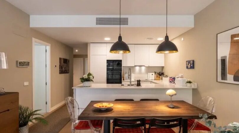 Open-plan kitchen with white fitted kitchen, dining table and black pendant lights in new ground-floor apartment La Vileta
