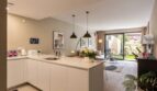 Open kitchen with white kitchen island and view into living room with garden access, new ground-floor apartment Palma