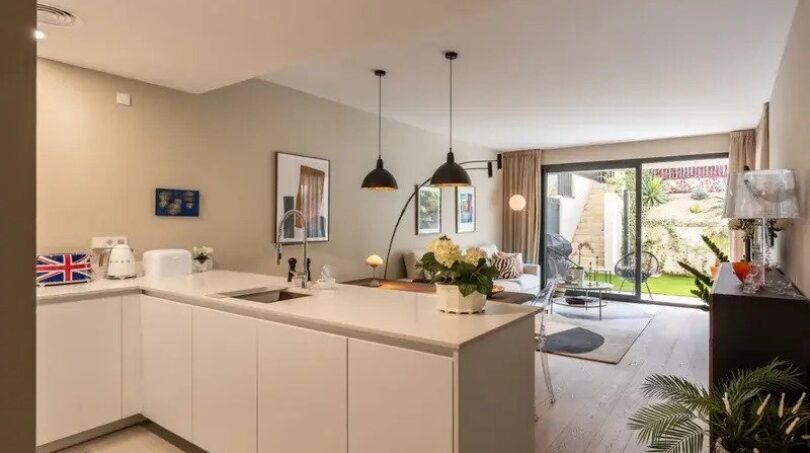 Open kitchen with white kitchen island and view into living room with garden access, new ground-floor apartment Palma
