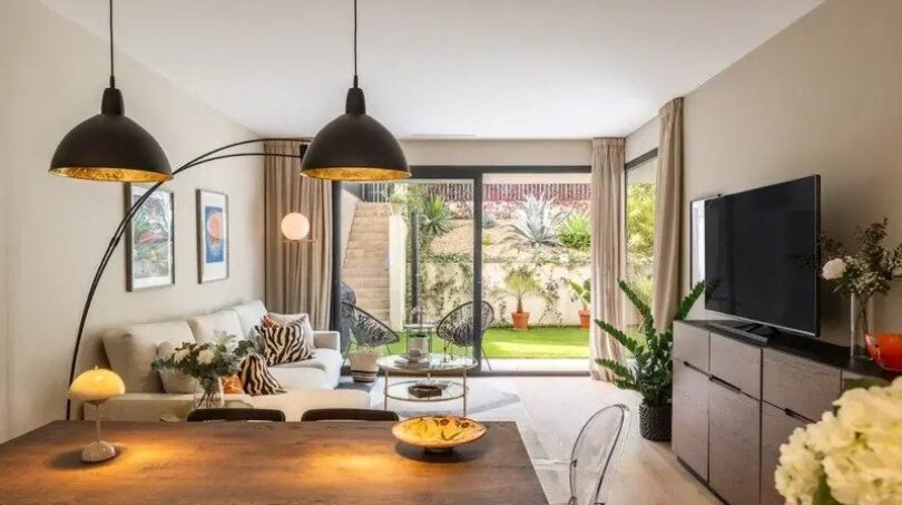 Bright living-dining area with wooden table, black pendant lights and access to the green garden