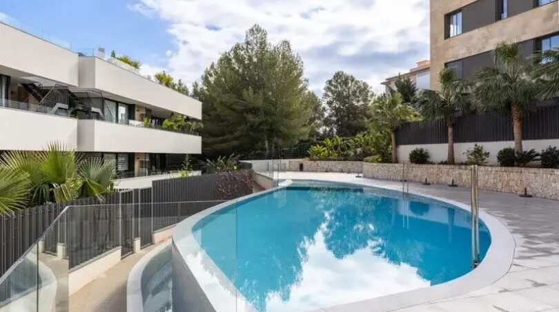 Oval outdoor pool with glass railing and modern residential buildings in the new La Vileta complex, Palma