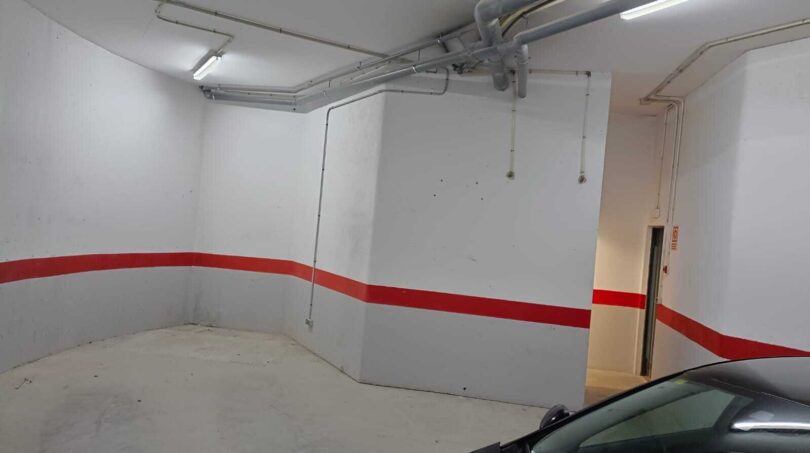 Underground garage of the townhouse in La Vileta with white walls, red stripe, concrete floor and parking space for cars.