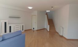 Helles Wohnzimmer mit Holzboden, blauem Sofa, weißer Kommode und offener Treppe ins Obergeschoss.