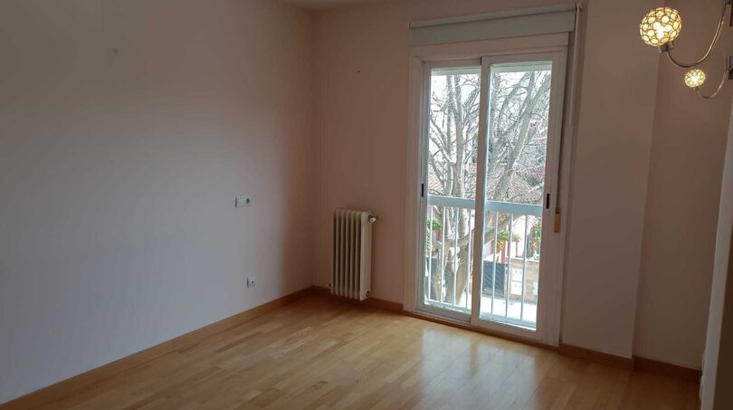 Bright, empty room with wooden floor, radiator and balcony door in the La Vileta townhouse, Palma