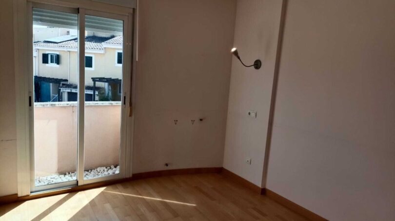 Bright empty bedroom with wooden floor, wall light and glass sliding door to the balcony in the La Vileta townhouse
