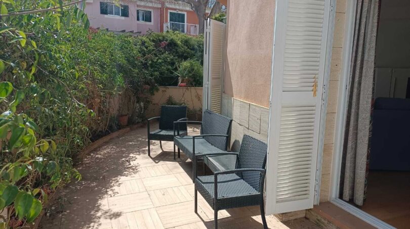 Sunny terrace with rattan furniture, surrounded by green plants, with access to the living area of the townhouse in La Vileta.