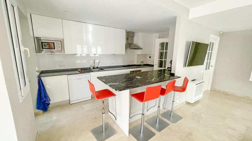 Moderne Küche mit weißen Hochglanzschränken, schwarzer Marmorarbeitsplatte und roten Barhockern im Apartment El Toro