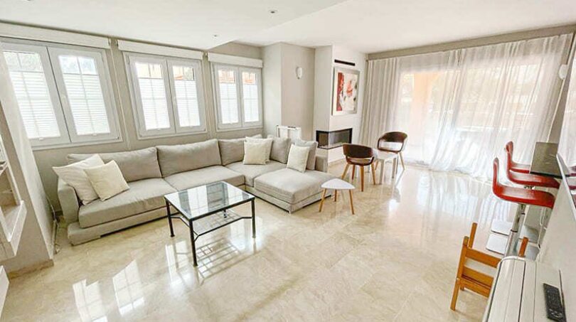 Helles Wohnzimmer mit grauem Ecksofa, Marmorboden, Glastisch und großen Fenstern im Apartment El Toro