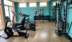 Moderner Fitnessraum mit Cardiogeräten, Hanteln und Cable-Machine, türkisfarbene Wände, Holzboden, Apartment El Toro