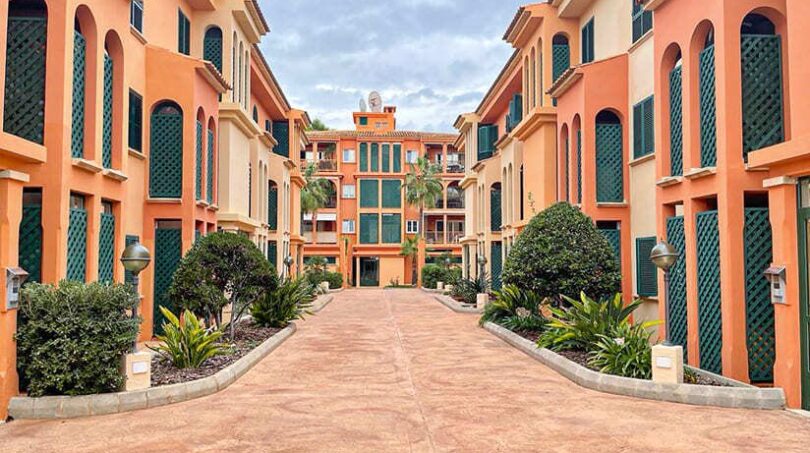 Mediterraner Innenhof einer Wohnanlage in El Toro mit orangefarbenen Fassaden, grünen Fensterläden und gepflegtem Grün.