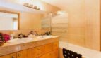 Helles Badezimmer mit Doppelwaschbecken, Holzunterschrank, Marmor-Ablage und Badewanne mit Glasabtrennung.