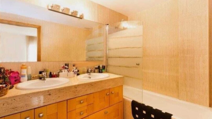 Helles Badezimmer mit Doppelwaschbecken, Holzunterschrank, Marmor-Ablage und Badewanne mit Glasabtrennung.