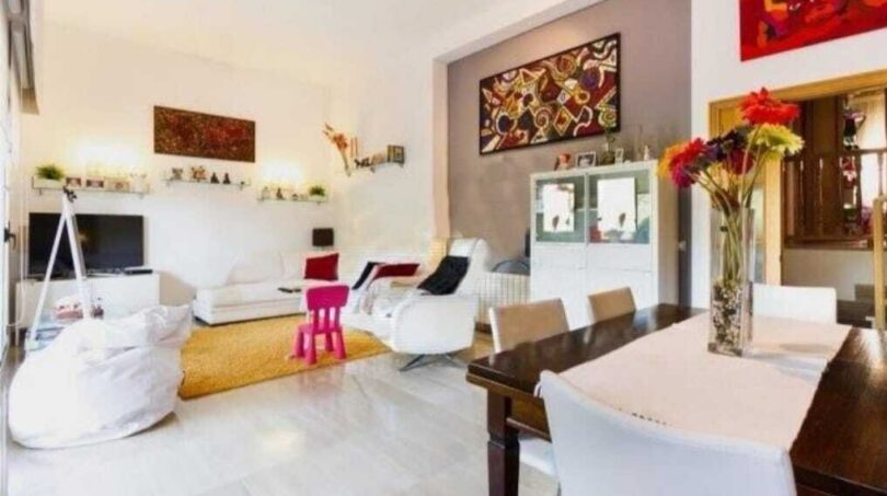 Helles Wohnzimmer mit Esstisch, bunten Kunstwerken, weißen Möbeln und orangem Teppich in Palma de Mallorca