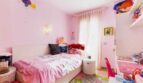 Kinderzimmer in Rosa mit Einzelbett, Spielzeug, buntem Teppich und Fenster mit Vorhängen in Palma de Mallorca.