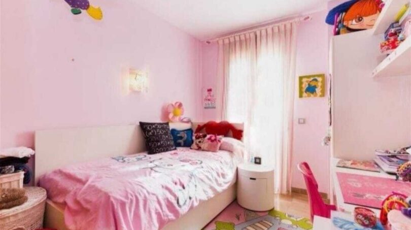 Kinderzimmer in Rosa mit Einzelbett, Spielzeug, buntem Teppich und Fenster mit Vorhängen in Palma de Mallorca.