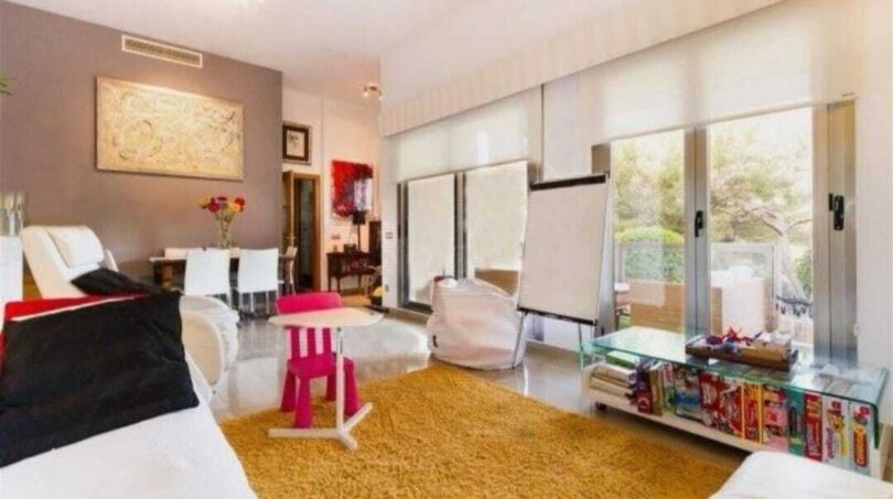 Helles Wohnzimmer mit goldfarbenem Teppich, Glasfront zur Terrasse und modernem Kinderspielbereich in Palma