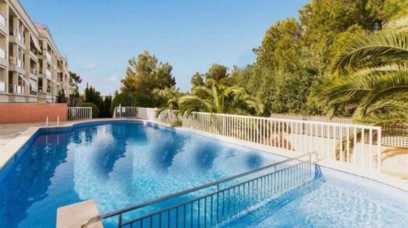 Gemeinschaftspool mit weißem Zaun, Palmen und mehrstöckigem Wohngebäude in Palma de Mallorca