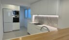 Moderne weiße Küche mit Marmoroptik-Rückwand, Inseltheke aus Holz und integrierten Bosch-Geräten im Penthouse Palma