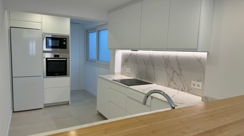 Moderne weiße Küche mit Marmoroptik-Rückwand, Inseltheke aus Holz und integrierten Bosch-Geräten im Penthouse Palma