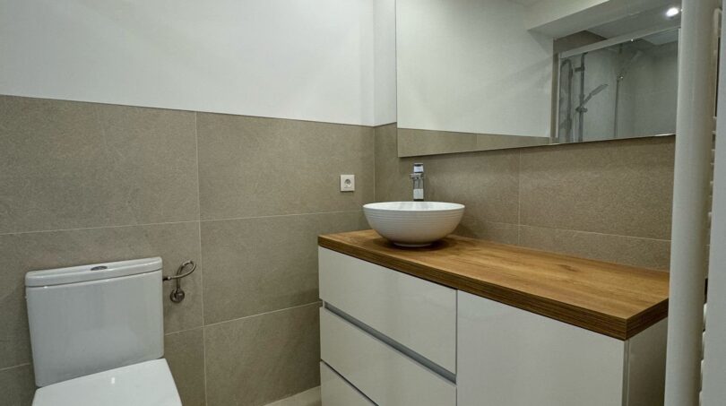 Modernes Badezimmer mit weißem Waschtischunterschrank, Holzabdeckung, Aufsatzwaschbecken und beigen Wandfliesen im Penthouse Palma