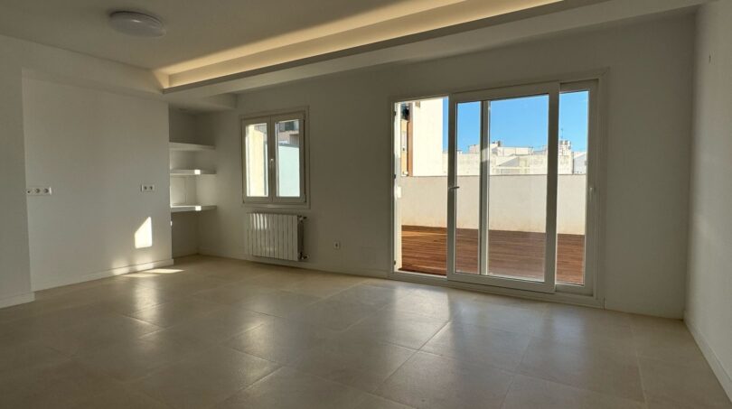 Helles, leeres Wohnzimmer mit Terrassenzugang, Betonboden und indirekter Beleuchtung im Penthouse Palma