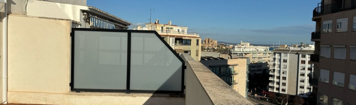 Sonnige Dachterrasse mit Holzboden, Glastrennwand und Panoramablick über Palma de Mallorca bei blauem Himmel.