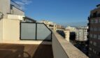 Sonnige Dachterrasse mit Holzboden, Glastrennwand und Panoramablick über Palma de Mallorca bei blauem Himmel.