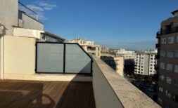 Sonnige Dachterrasse mit Holzboden, Glastrennwand und Panoramablick über Palma de Mallorca bei blauem Himmel.