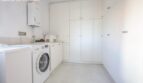 Modern laundry room with washing machine, boiler and white built-in cabinets in the chalet in Puerto Adriano