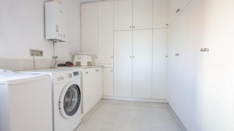 Modern laundry room with washing machine, boiler and white built-in cabinets in the chalet in Puerto Adriano
