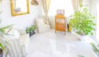 Bright living room of the chalet in Puerto Adriano with white tiles, armchairs and lush houseplants.