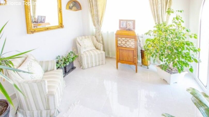 Bright living room of the chalet in Puerto Adriano with white tiles, armchairs and lush houseplants.