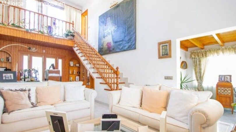 Bright living room with white sofas, wooden staircase, gallery and large artwork in Puerto Adriano chalet