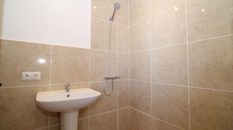 Helles Badezimmer der Finca mit beiger Fliesendusche, Handbrause und Waschbecken auf Säule.
